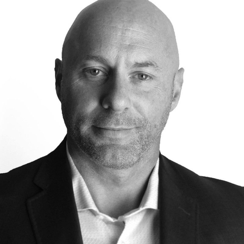 Professional headshot of a bald man in a suit against a white background.